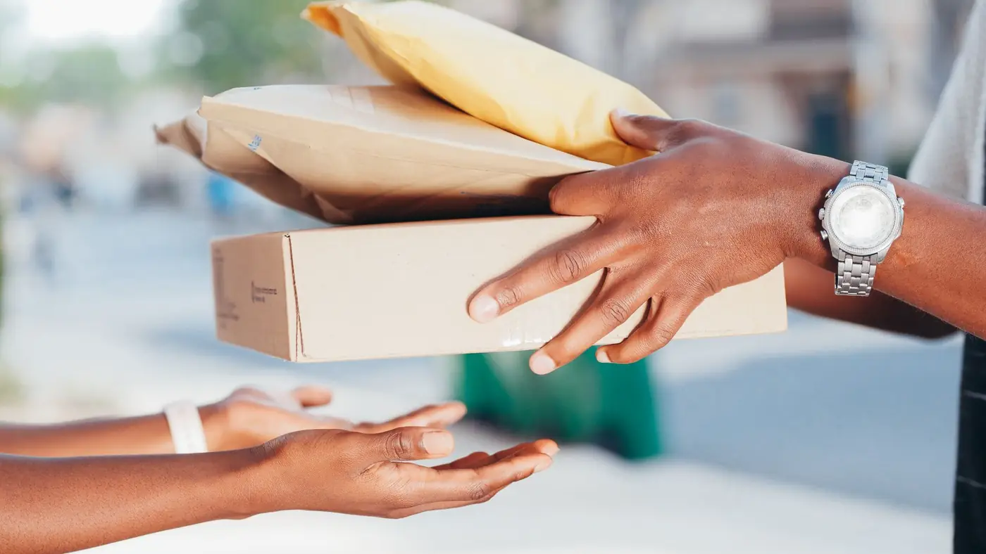 One person handing a wrapped package and a box to another, close up on their hands