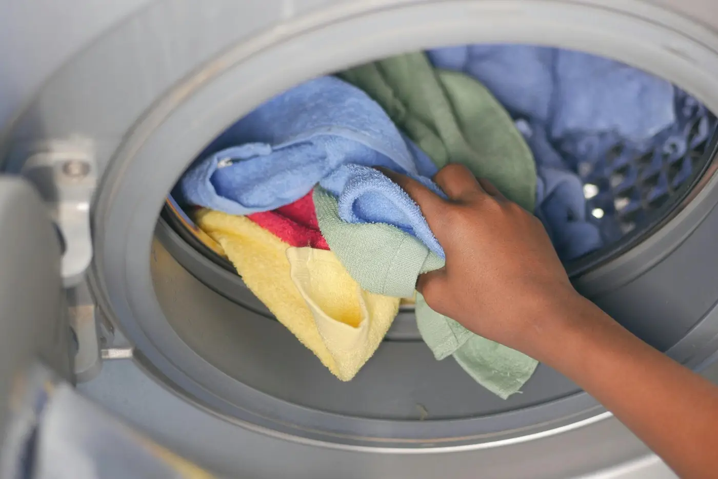 A hand loading colourful towels into a front-load washing machine