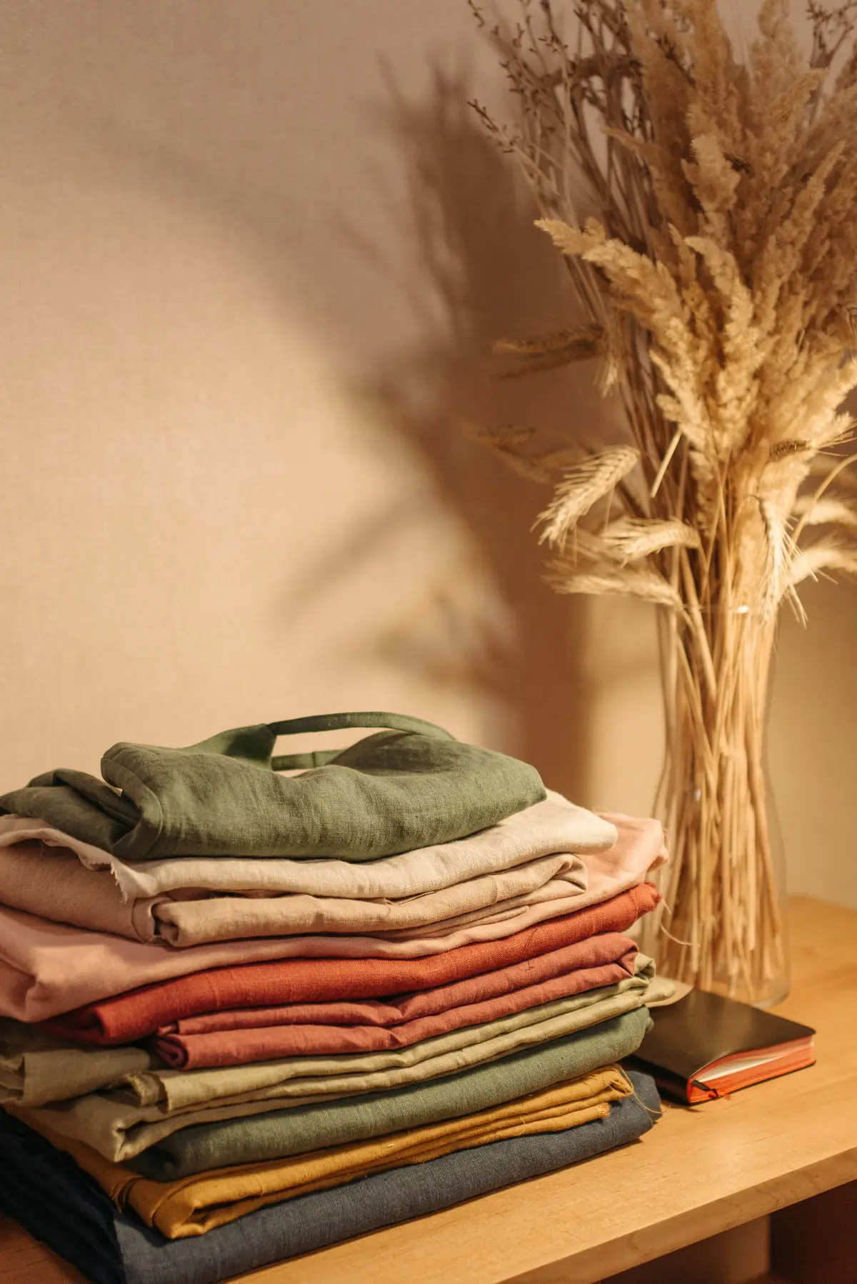A neat stack of folded linen clothes in green, cream and rust on a wooden table